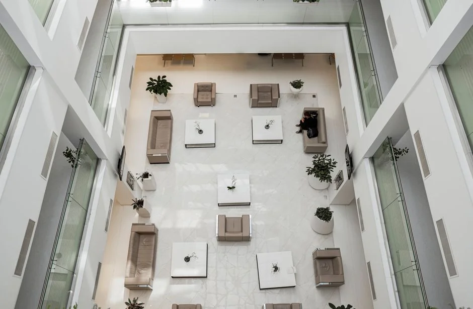 Une main utilisant un plumeau pour dépoussiérer un bureau en bois, entouré de plantes et d’objets de bureau.