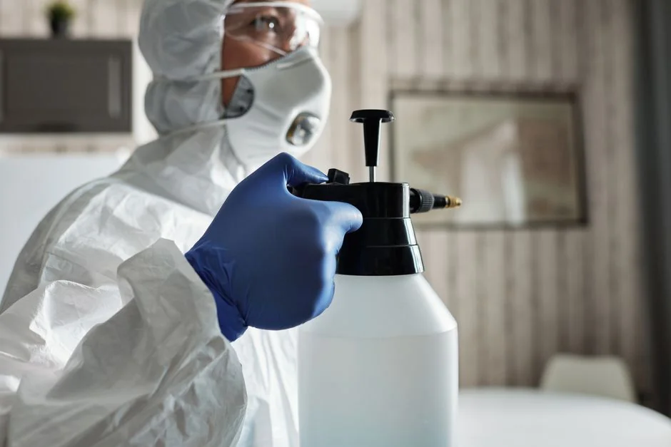 An individual disinfects a workspace using fumigation, wearing full protective gear for safety.